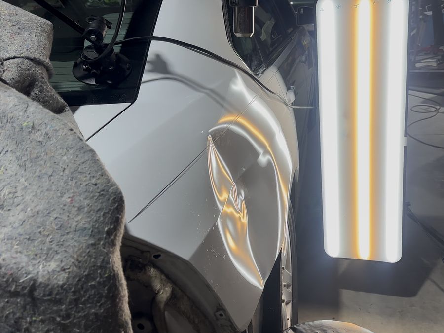 Minor collision damage dent on a car fender before paintless dent repair
